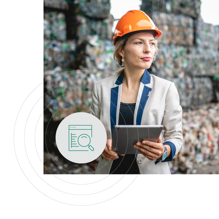 Female worker wearing an orange safety helmet and holding a tablet, standing in front of stacked recyclable waste materials, symbolizing the use of technology for waste management.